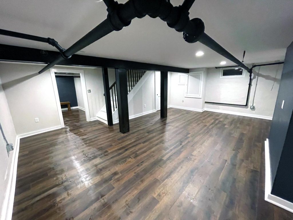 Recently renovated basement with hardwood floors, bright walls and black accent beams