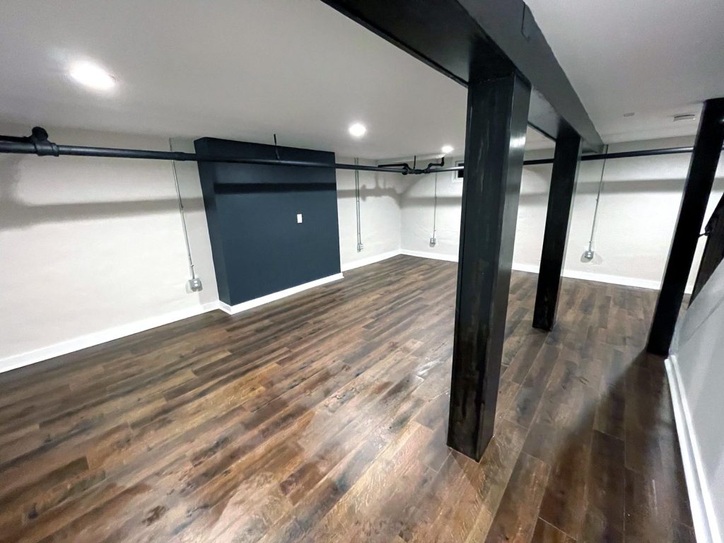 Basement with hardwood floors, bright walls, black beams and a blue accent wall