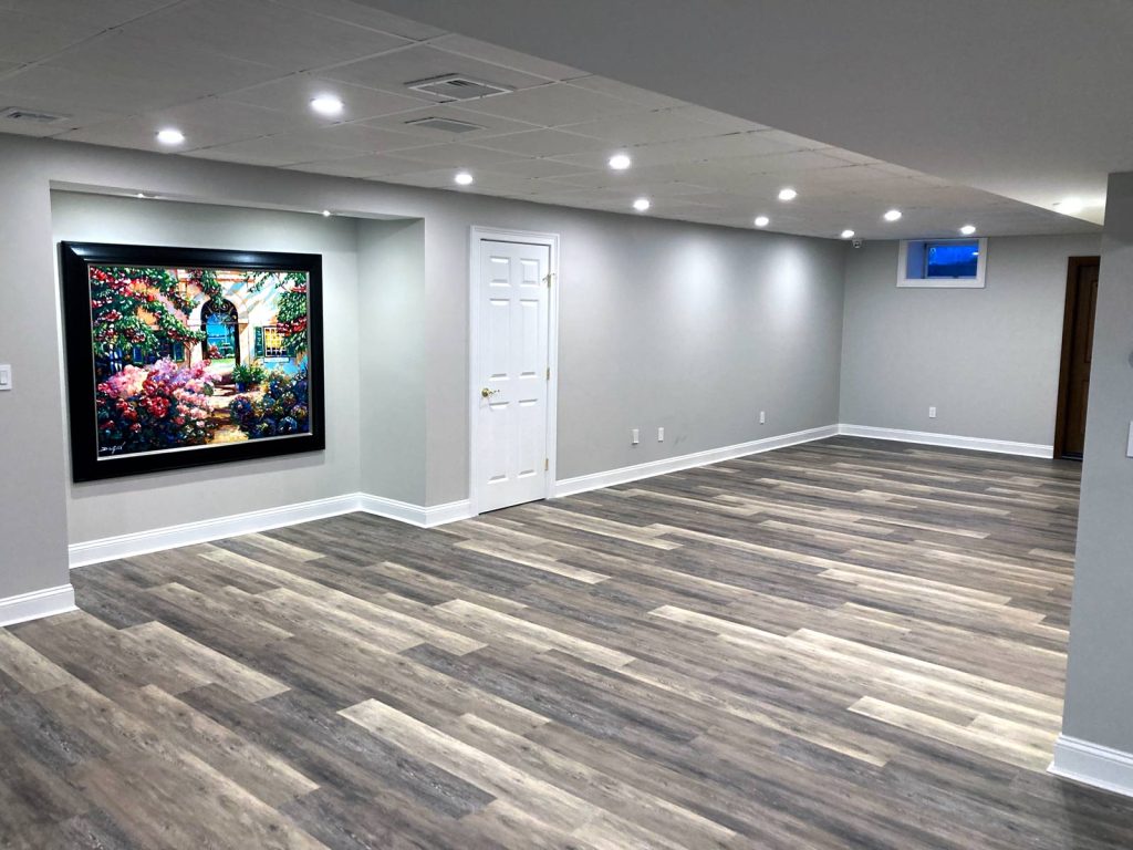 A finished basement with grey walls, recessed lighting and wood floors by White Maple Construction