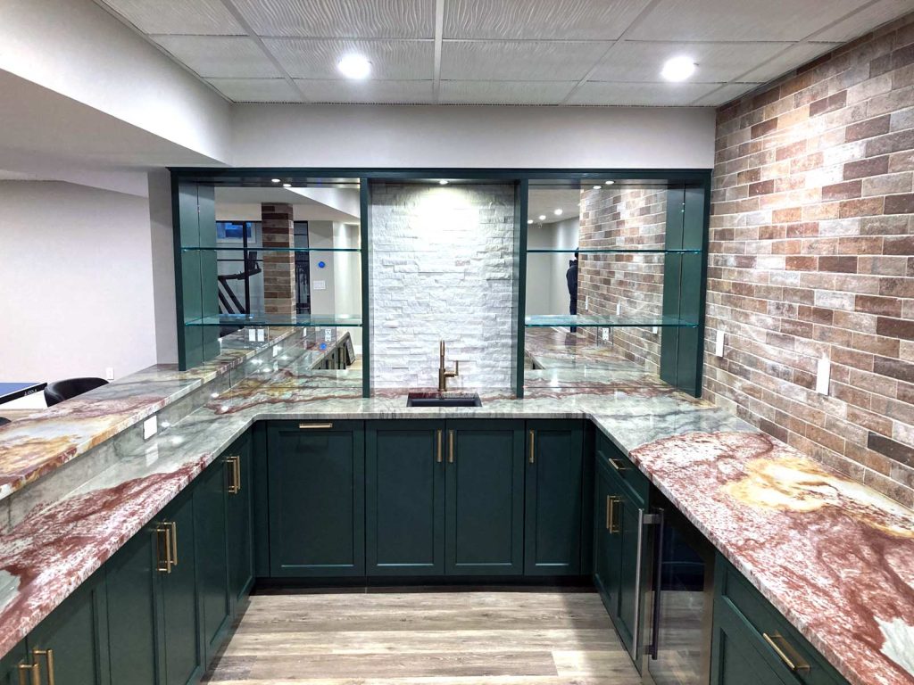 A basement wet bar with striking green cabinets and colorful marbled countertops by White Maple Construction