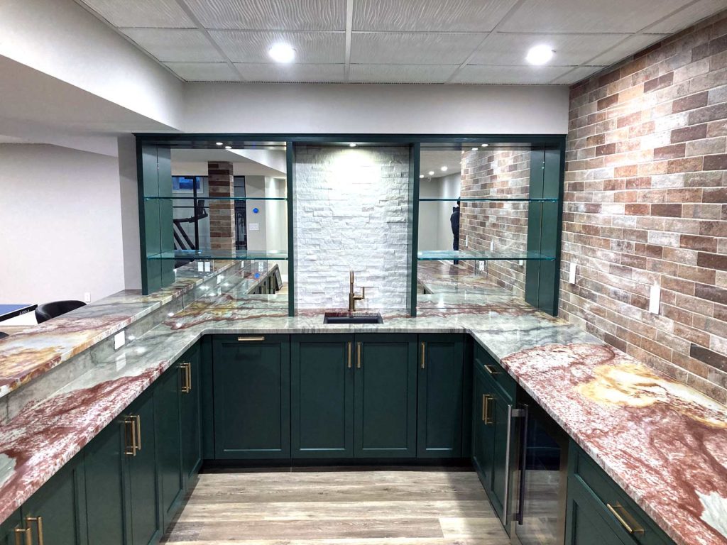 A gorgeous basement wet bar remodel with green cabinets and marbled countertops by White Maple Construction