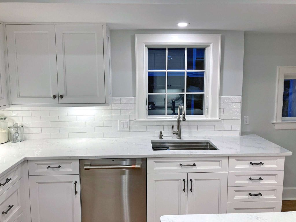 A modern white kitchen renovation with white marble countertops and white subway tiles by White Maple Construction